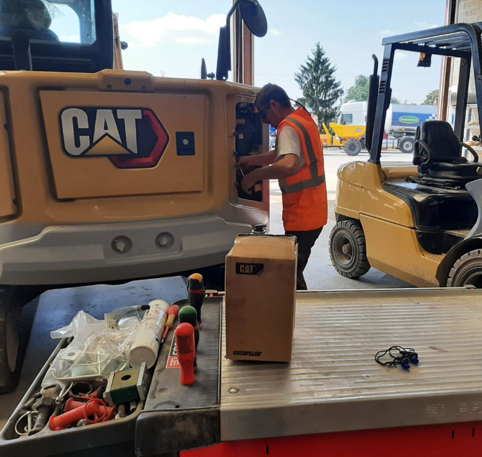 Technicien de chez Stage location TP au travail sur une mini pelle compacte Caterpillar dans l'atelier